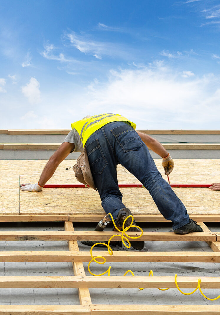 Concept of building new wood or wooden house. Two mature and professional worker standing on roof top of new modern house under construction. Roofer using level and measuring size of the rooftop cover